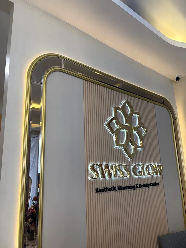 Logo Swiss Glow emas backlit di dinding kayu slat