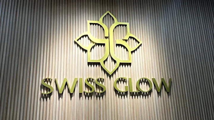 Emblem dan tulisan Swiss Glow berwarna emas pada dinding panel kayu
