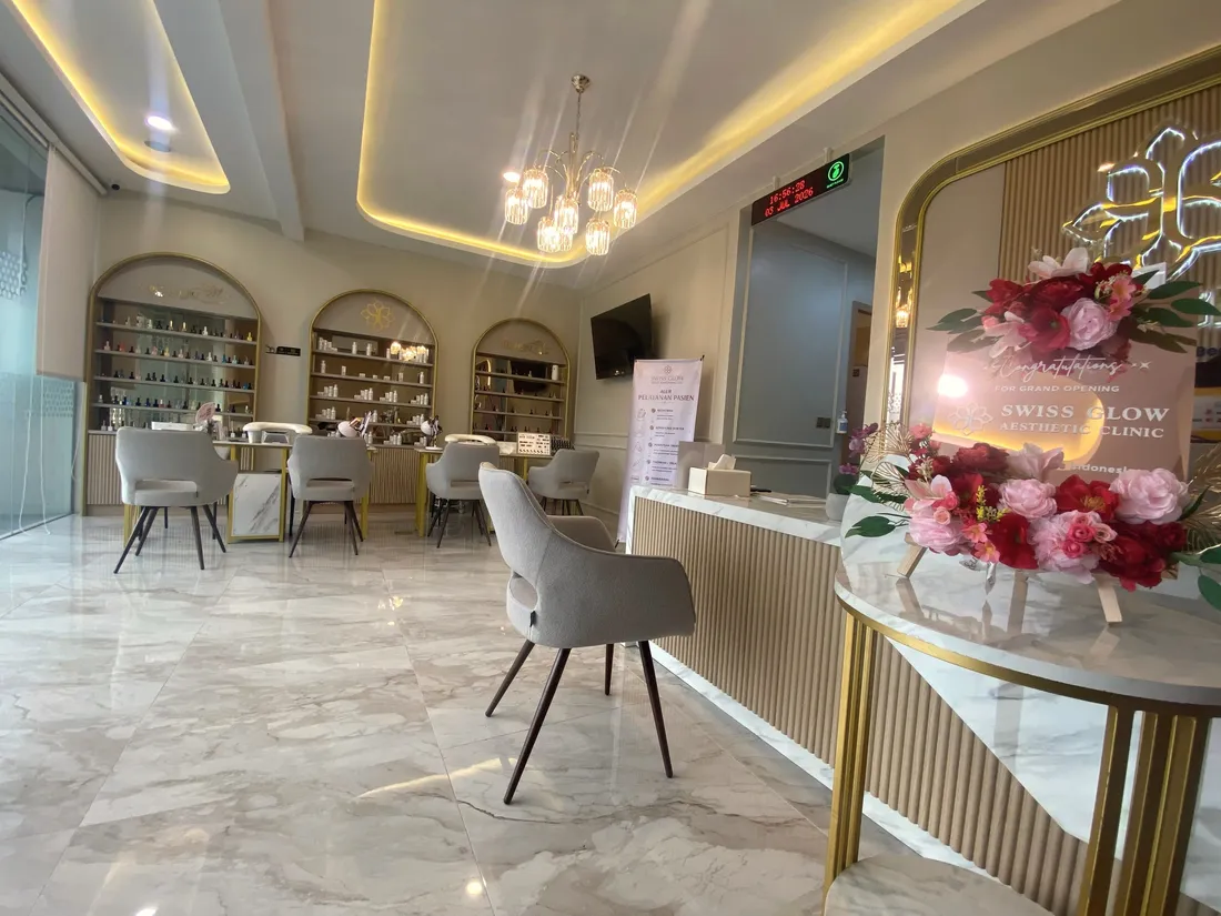 Lounge Swiss Glow dengan lantai marmer, chandelier kristal, rak arch berbingkai emas, dan meja resepsionis berpanel kayu slat